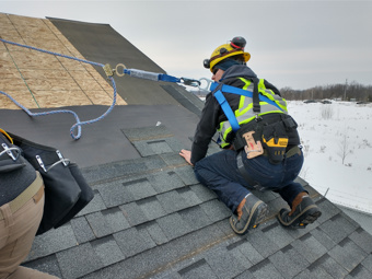 construction student on the roof of a house being built and practicing laying shingles