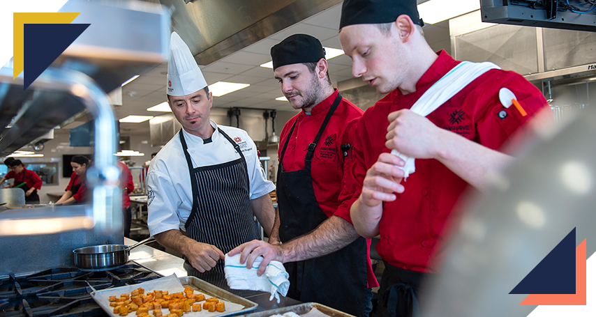 Instructor inspecting two culinary students' meal
